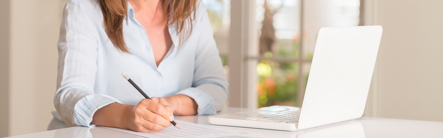 Frau sitzt vor Laptop am Tisch und macht sich Notizen