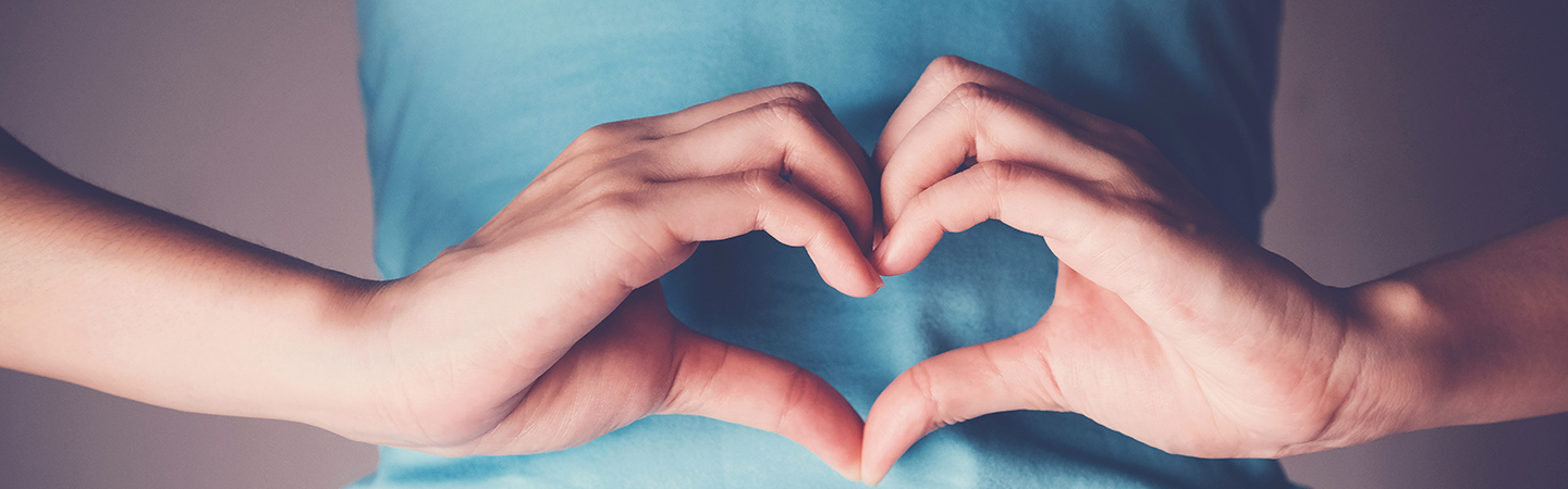 Frau macht Herz-Symbol vor dem Bauch