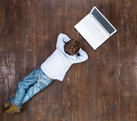 Kind liegt bäuchlings auf dem Boden und schaut auf einen Lapotp