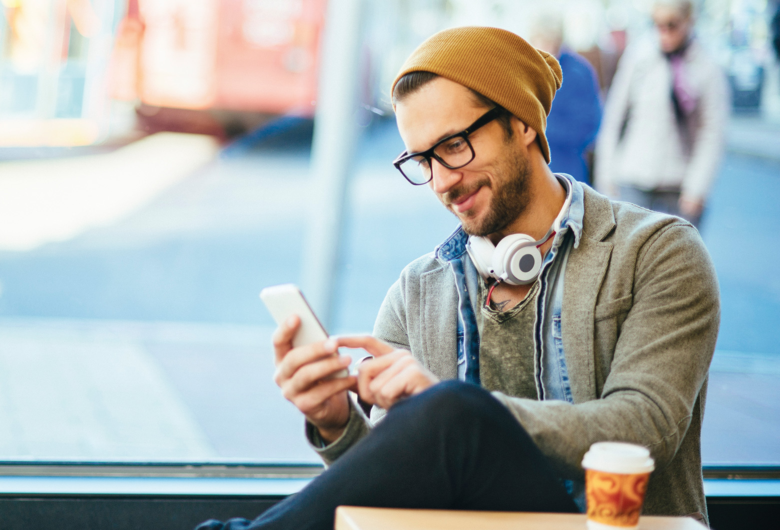 Junger Mann trinkt Kaffee und schaut auf sein Smartphone.