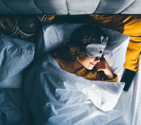 Junge Frau im Bett mit Schlafmaske