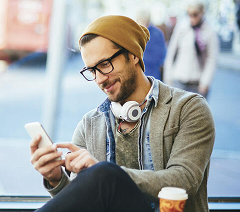Junger Mann trinkt Kaffee und schaut auf sein Smartphone.