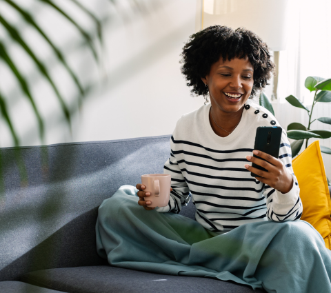 Frau auf der Couch entspannt mit dem Smartphone.